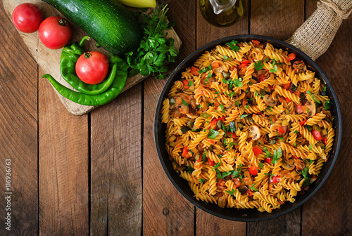 Vegetarian Vegetable pasta Fusilli with zucchini, mushrooms and capers in pan on wooden table. Top view