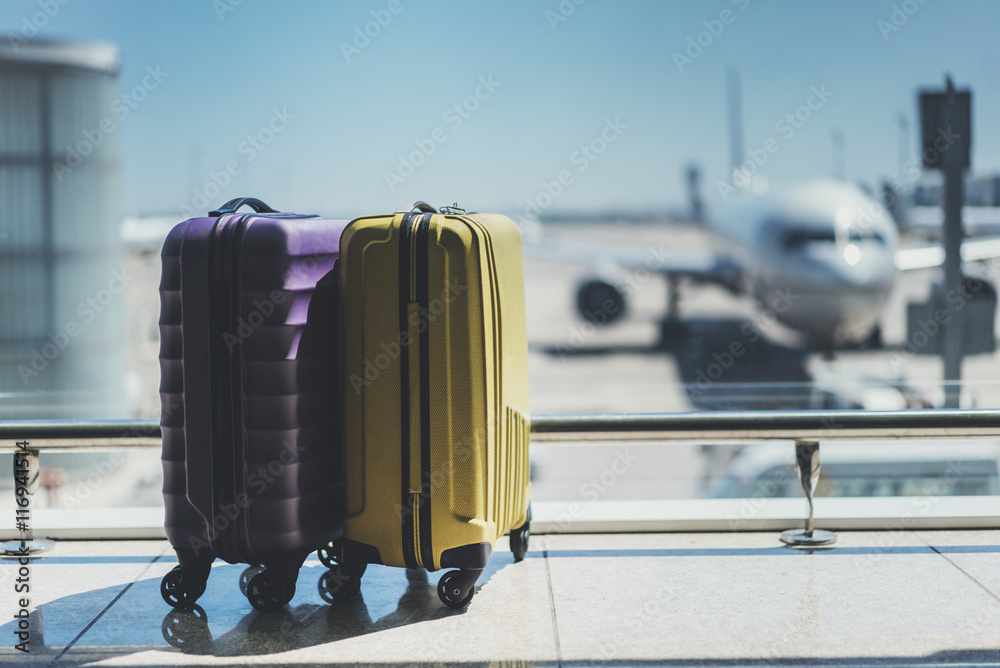 Two suitcases in the airport departure lounge, airplane in the blurred background, summer vacation concept, traveler suitcases in airport terminal waiting area - obrazy, fototapety, plakaty 