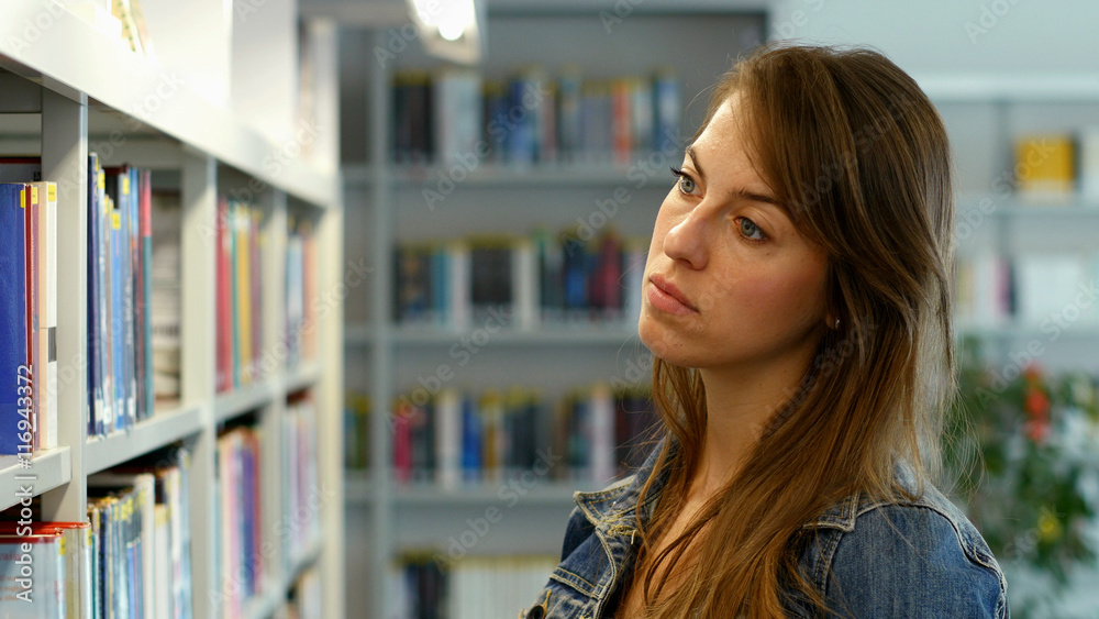 A young woman in a public library. It's her leisure time and she is looking for some good books to read. A young woman in a public library. It's her leisure time and she is looking for some good books to read.