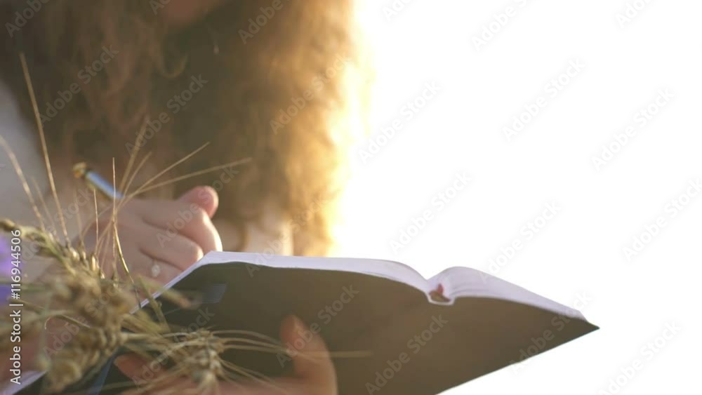Female hands with pen writing on notebook on grass outside