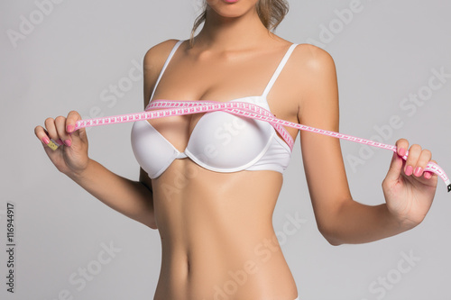Sporty woman measuring up her chest, isolated in gray, in white lingerie or underwear fashion and beauty spa massage