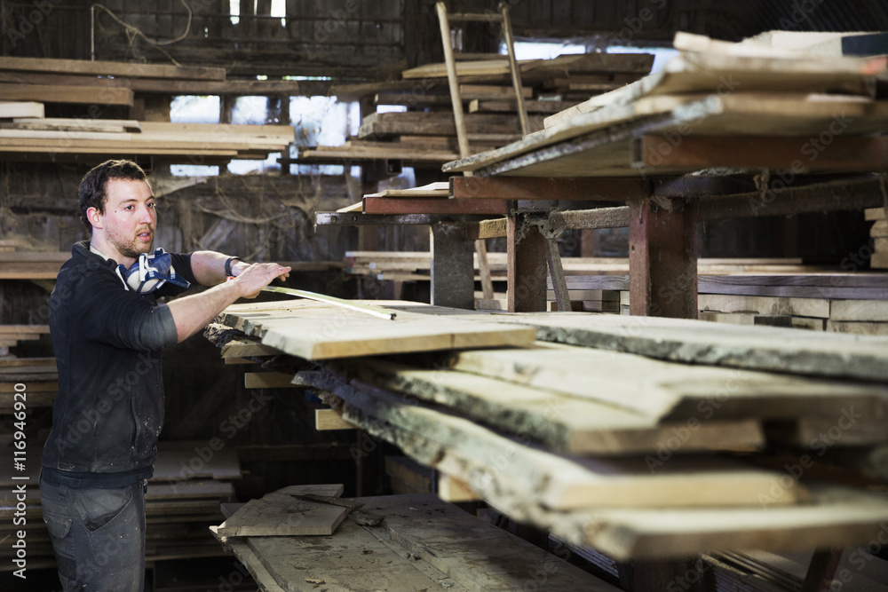 Man working in a carpentry workshop, measuring a plank of wood. Man working in a carpentry workshop, measuring a plank of wood.