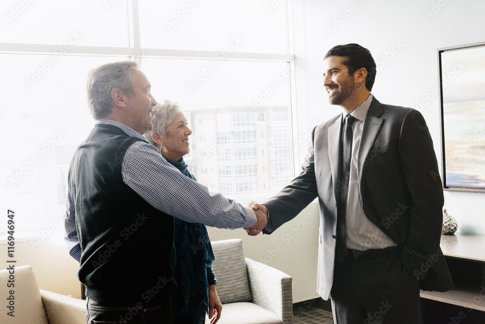 A man greeting a mature couple in an office. A man greeting a mature couple in an office.