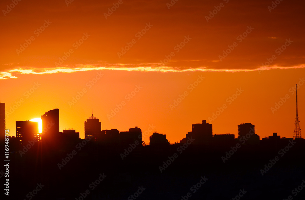 Glowing orange sun setting behind city buildings in silhouette (North Sydney, Australia)