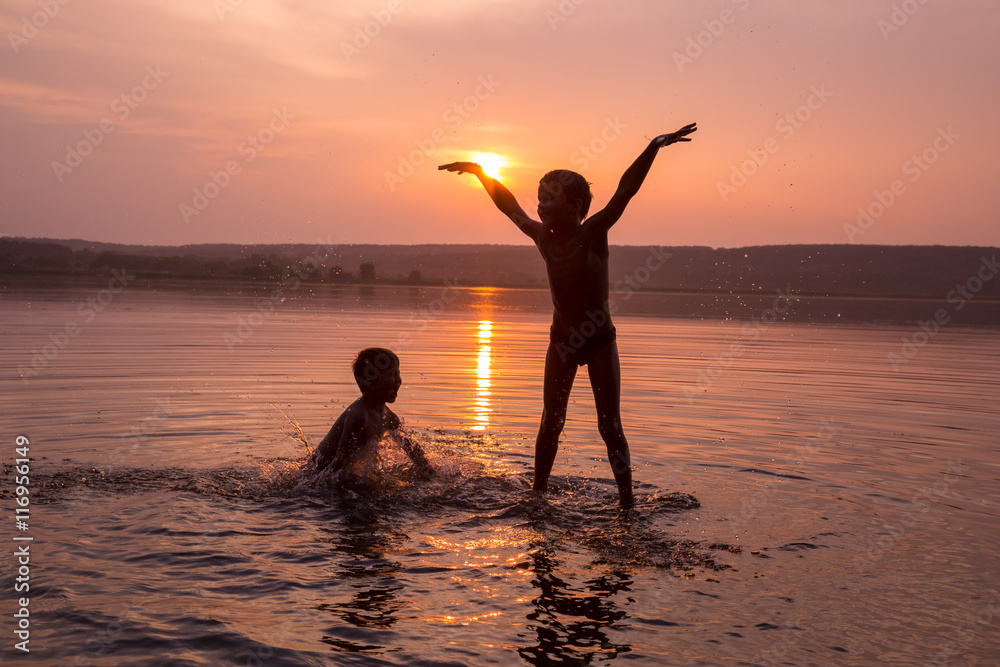 Fototapeta premium Two boys jumping into water on sunset