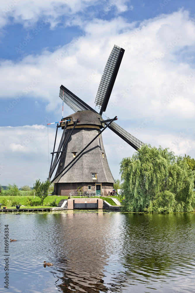 Ancient wind mill reflected in a blue canal on a summer day at Kinderdijk, Netherlands