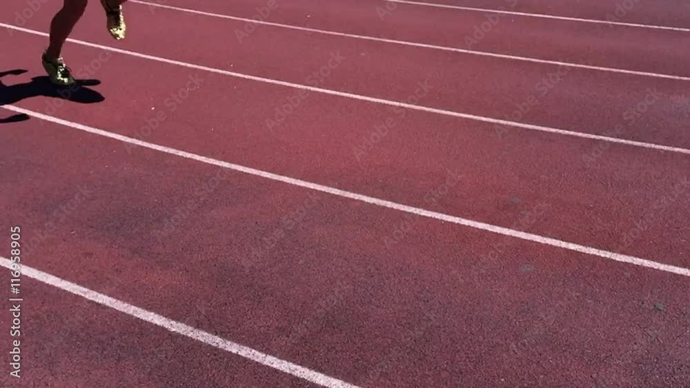 Athlete in gold shoes sprinting in slow motion on rustic red running track Athlete in gold shoes sprinting in slow motion on rustic red running track