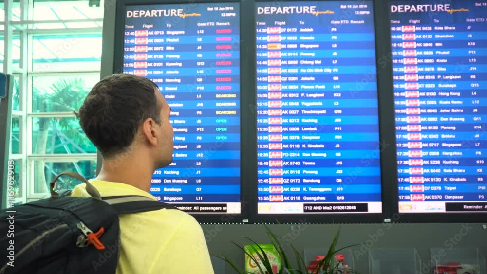 Male traveler backpacker looking at airport schedule screen