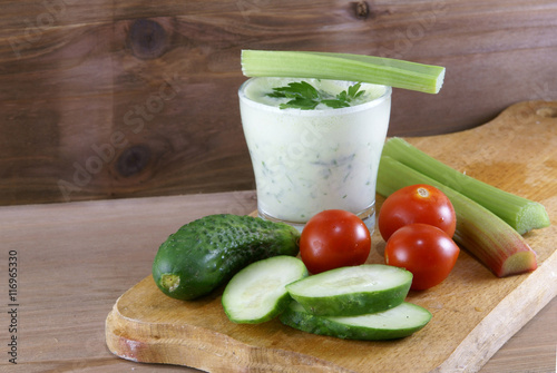 Useful summer snack: vegetables and yogurt sauce with herbs. Against the background of a rustic wooden table