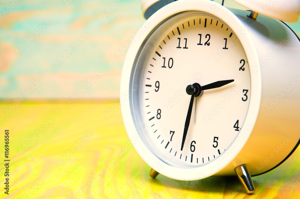 White alarm clock isolated on colorful wooden background