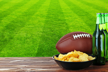Beer bottles, ball and snack on football field background
