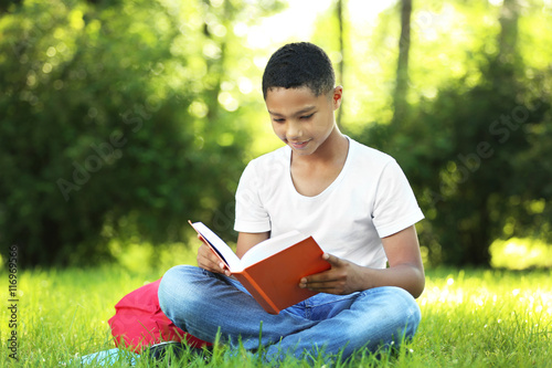 African American boy reading book in park