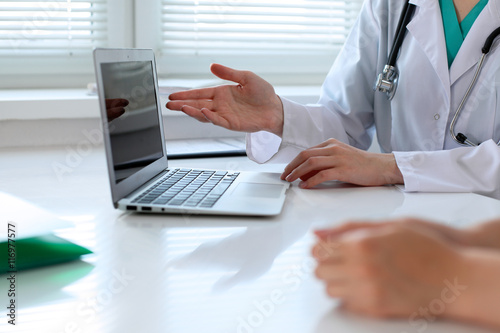 Doctor pointing into laptop computer and discussing something with her patient. Close-up.