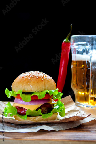 Homemade tasty beef burger with lettuce, ketchup, tomato, onions and cheese served on pieces of brown paper on a rustic wooden table of counter, with cold beer. Selective focus