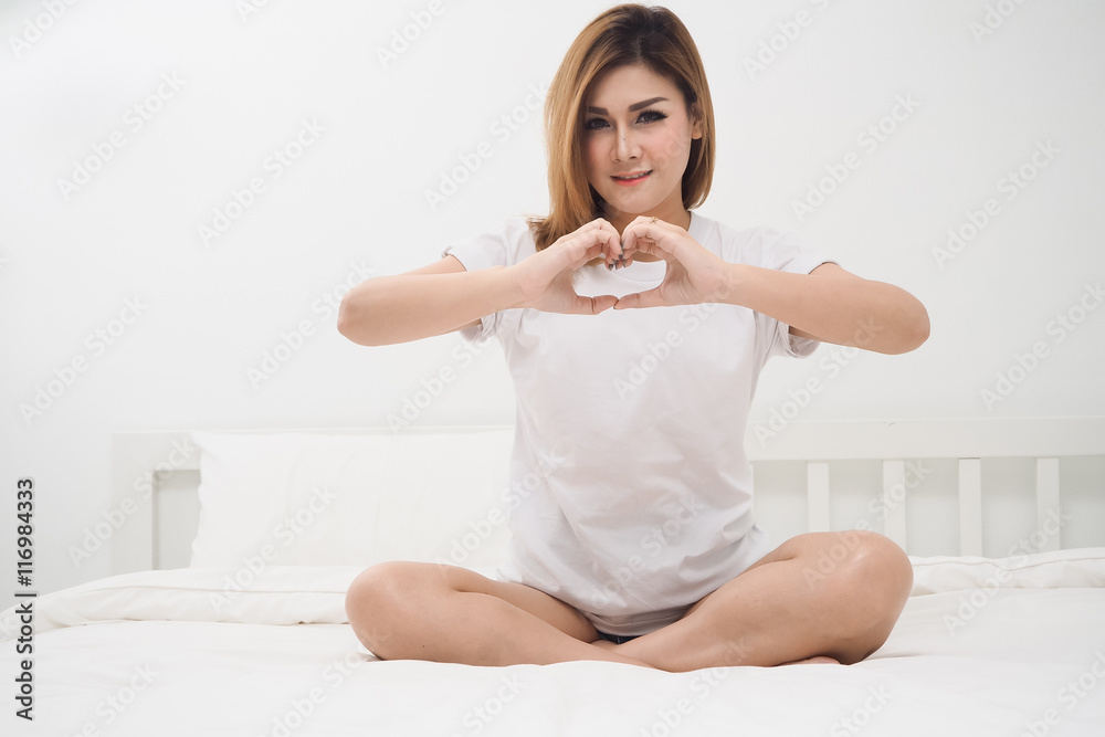 pretty woman holding hand symbol of heart shape on white bed pretty woman holding hand symbol of heart shape on white bed