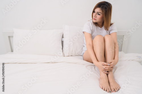 sadness woman sitting on white bed and looking something in bedroom