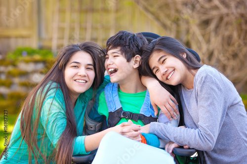 Sisters laughing and hugging disabled little brother in wheelcha