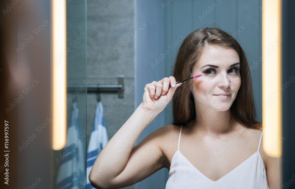 Woman applying mascara on long eyelashes in front of mirror Woman applying mascara on long eyelashes in front of mirror