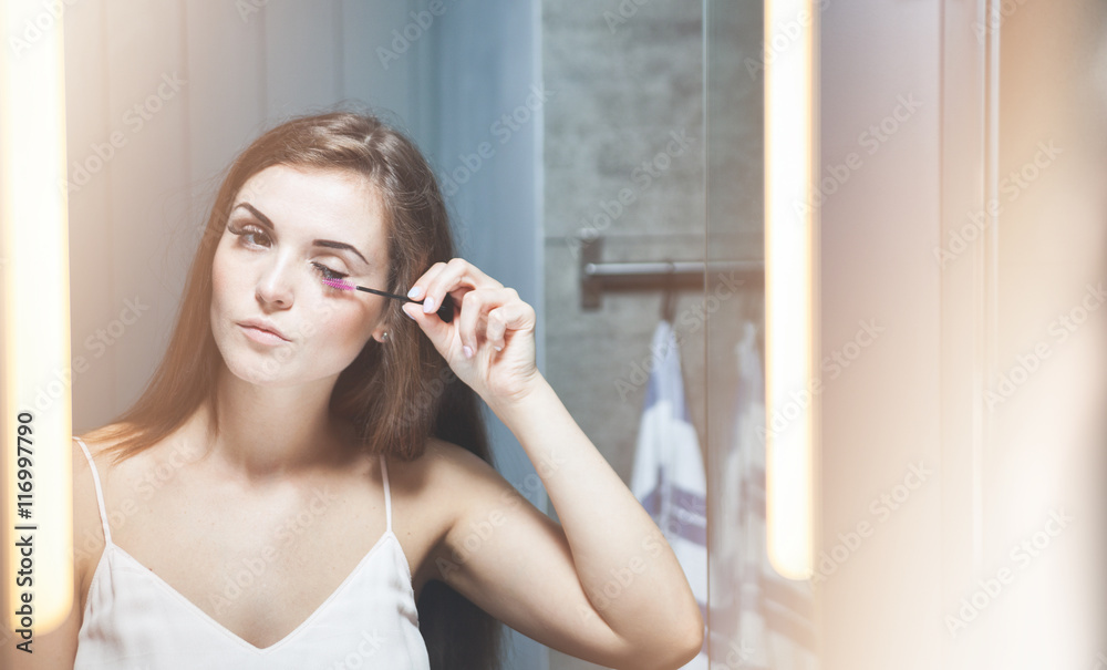 Woman applying mascara on long eyelashes in front of mirror Woman applying mascara on long eyelashes in front of mirror