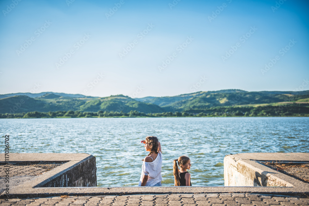 Two girls standing on river dock and looking sideways