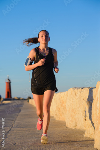 Fototapeta Naklejka Na Ścianę i Meble -  Young sporty girl running alone at beautiful sunset near the lig