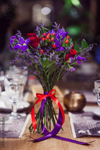 Flowers composition in restaurant, small red roses and purple irises, combination of multiple colors