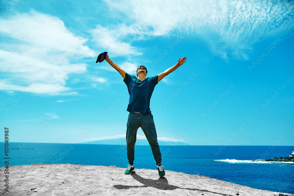 Happy stylish man in casual clothes standing on the cliff of mountain with raised hands to the sun and celebrating success Happy stylish man in casual clothes standing on the cliff of mountain with raised hands to the sun and celebrating success