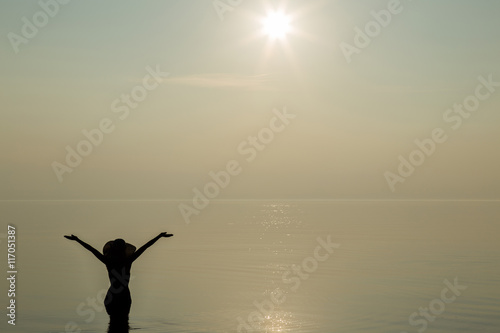 Silhouette. Young woman with hat on head enjoy the light sunset on the beach and she feels the freedom. Serene and warm, gentle water. In front of view opens infinity.