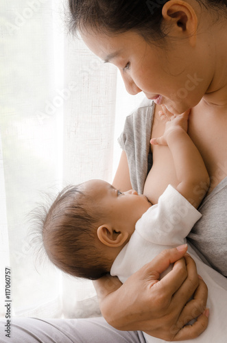 Mother breastfeeding her newborn baby beside window