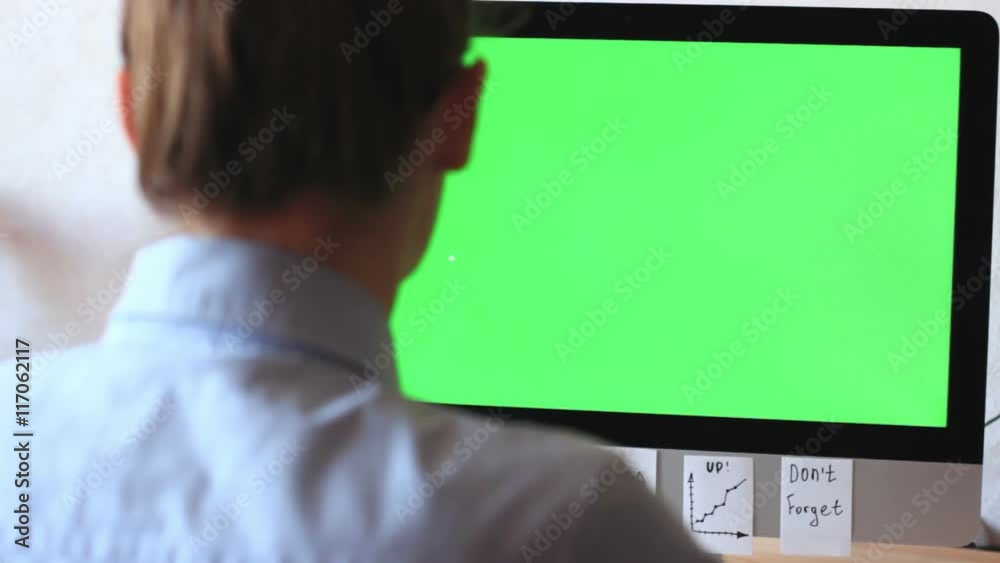 A freelancer working on a computer plastered with notes, reminders, stickers. On the monitor green screen, chroma key.