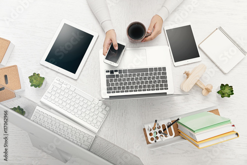 Concept of using electronics. Businesswoman works at office. Computer, laptop, tablet, cup of coffee and other things on the table. Top view