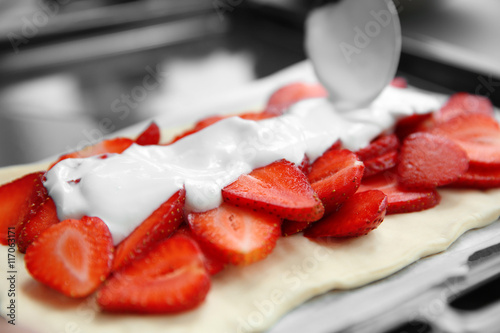 Pouring cream on strawberry dessert in oven tray