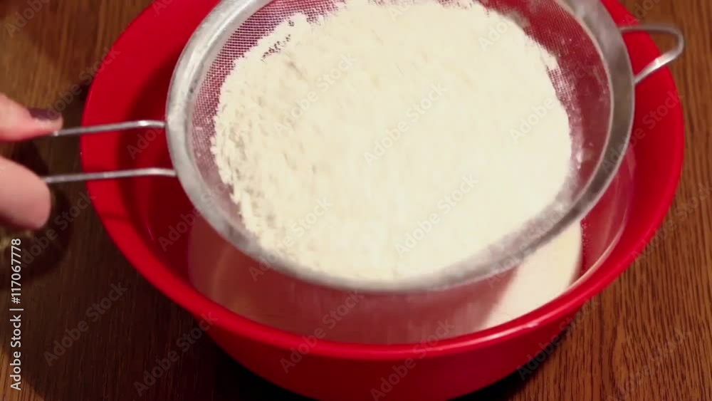 Woman uses a sieve to sift flour into a plastic bowl on a wooden table, close-up Woman uses a sieve to sift flour into a plastic bowl on a wooden table, close-up