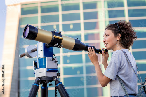 girl looking through a telescope outdoors
