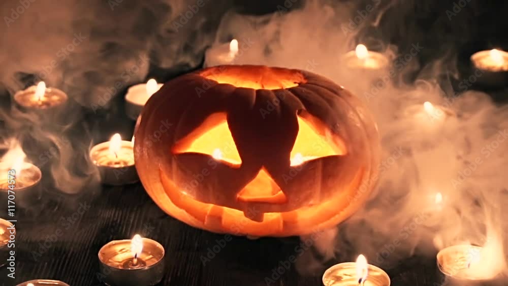 Carved Halloween pumpkin lit a flame inside, around the smoke travel along on a black background with lighted candles close up. Slowmotion Carved Halloween pumpkin lit a flame inside, around the smoke travel along on a black background with lighted candles close up. Slowmotion
