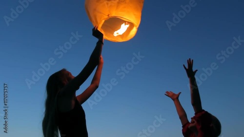 Two young girls launching a Chinese sky fly fire lantern to make a wish, summer holidays, celebration, family, children