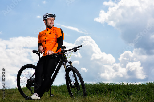 Young man cycling on a rural road through green meadow