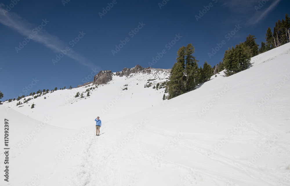 a lone female hiker ventures up the snowpack on the trail to Lassen Peak in Lassen Volcanic National Park in northern California