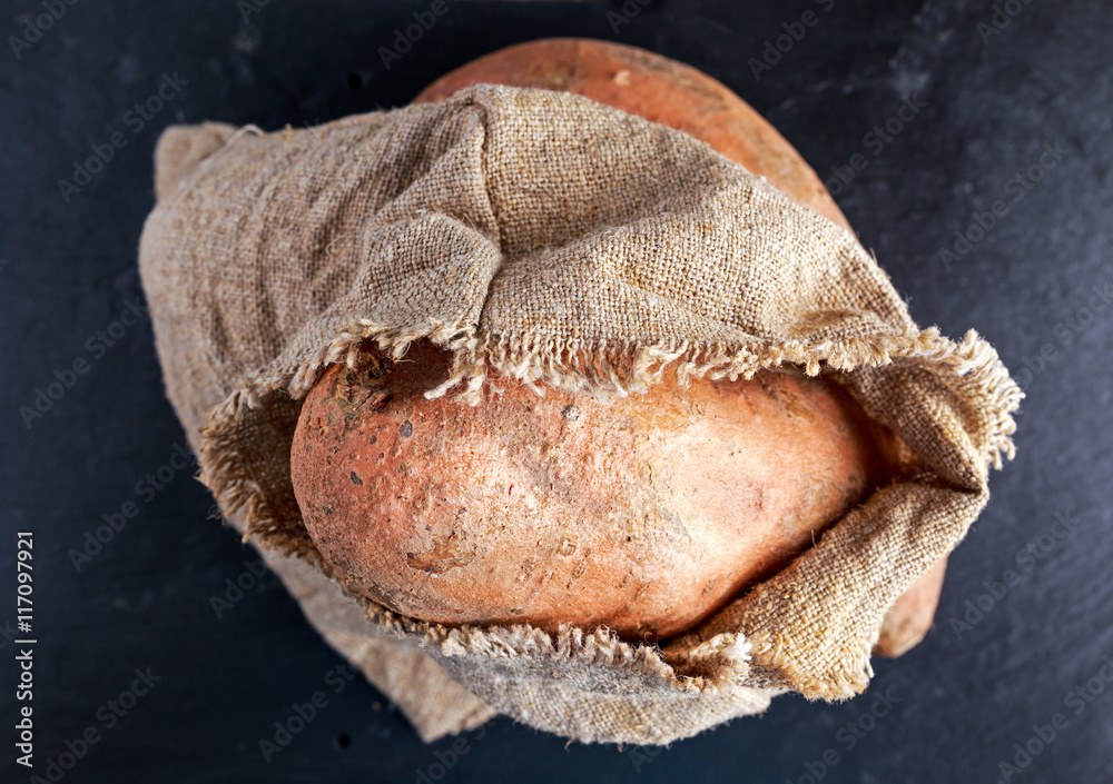 Obraz premium Freshly harvested organic sweet potatoes in a burlap bag on wooden table.
