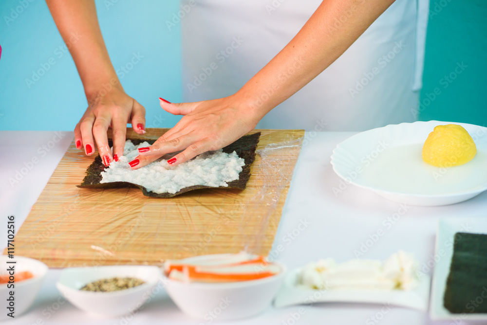 Hands of woman chef filling japanese sushi rolls with rice on a nori seaweed sheet.