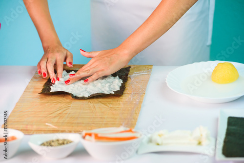Hands of woman chef filling japanese sushi rolls with rice on a nori seaweed sheet.