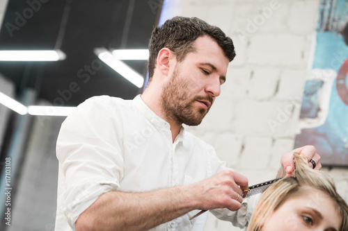 Hairdresser cutting client's hair in salon with electric razor closeup.