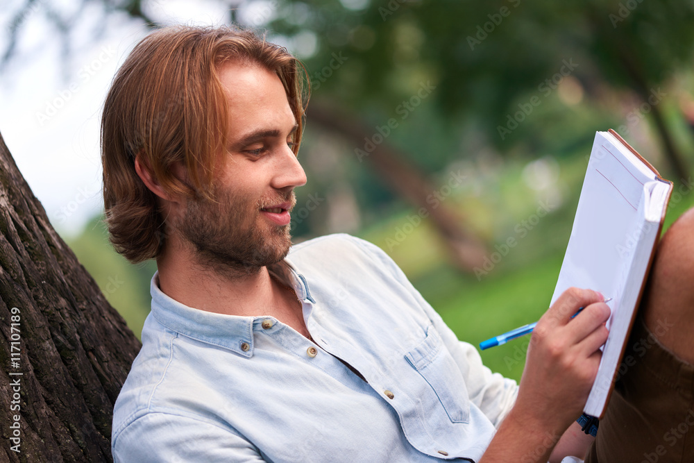 Fototapeta premium Smiling student in park of campus read a book
