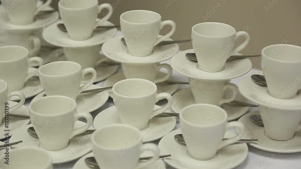 White cups with saucers and teaspoons are on table in several rows at banquet. White cups with saucers and teaspoons are on table in several rows at banquet.