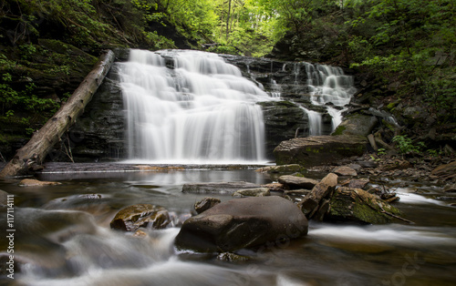 A long exposure of a medium sized waterfall in a lush green summer forest.
