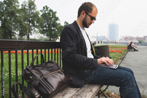 Businessman sitting on a wooden bench in the city using his laptop.
