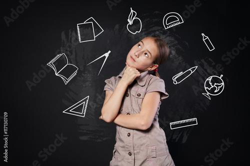 Small girl near chalkboard think of school subjects