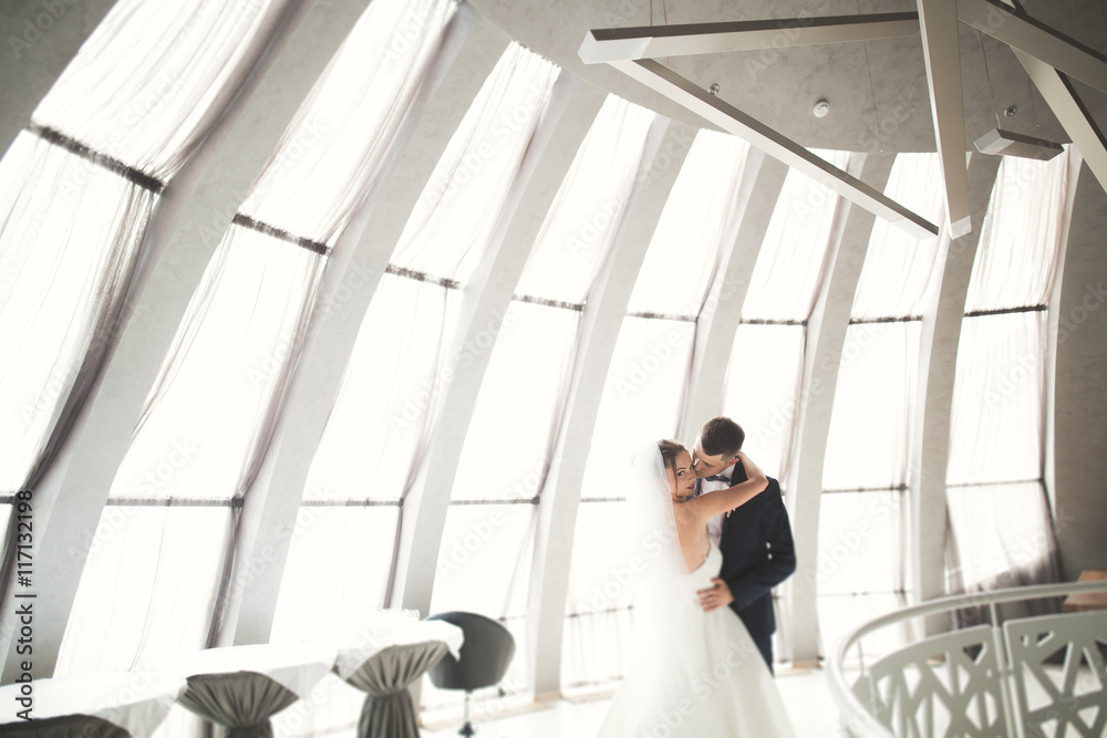 Lovely happy wedding couple, bride with long white dress posing in beautiful city Lovely happy wedding couple, bride with long white dress posing in beautiful city