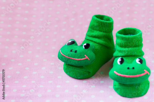 Pair of green socks with toys frogs for children closeup on spotted pink background, selective focus