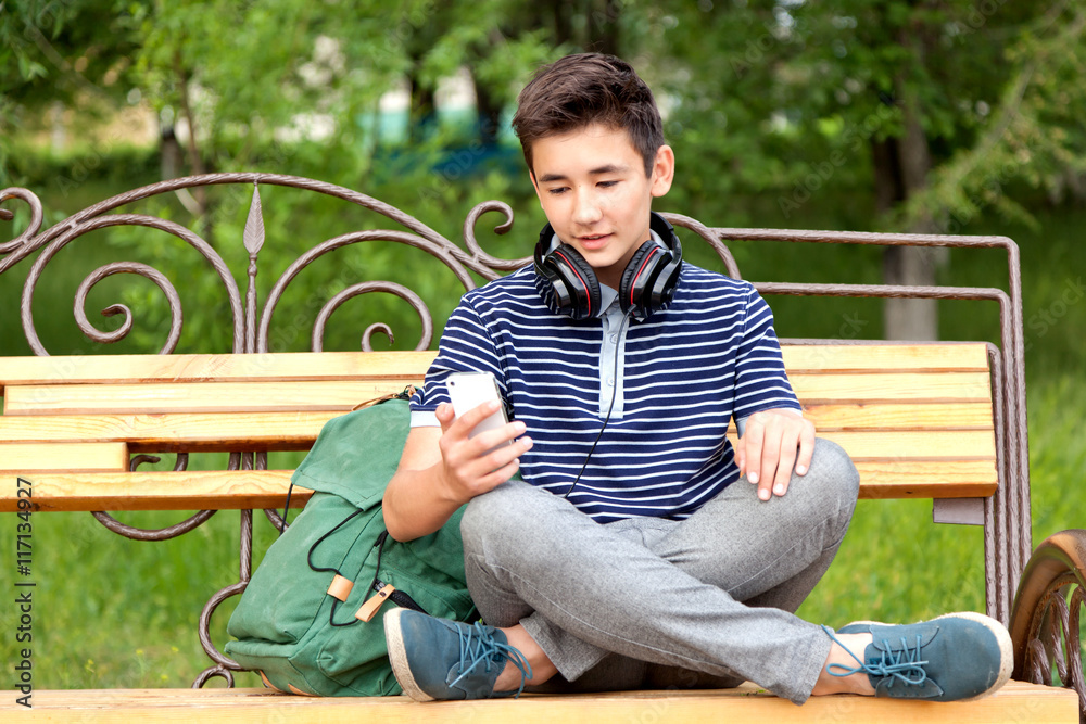 Obraz premium Asian teenager sitting on a bench with a school backpack, cell p